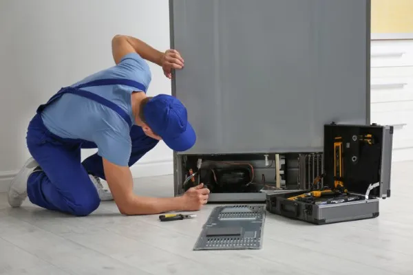 Hombre agachado reparando un refrigerador